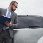 handsome businessman writing something to car insurance after car accident