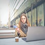 sad woman holding credit card while using laptop